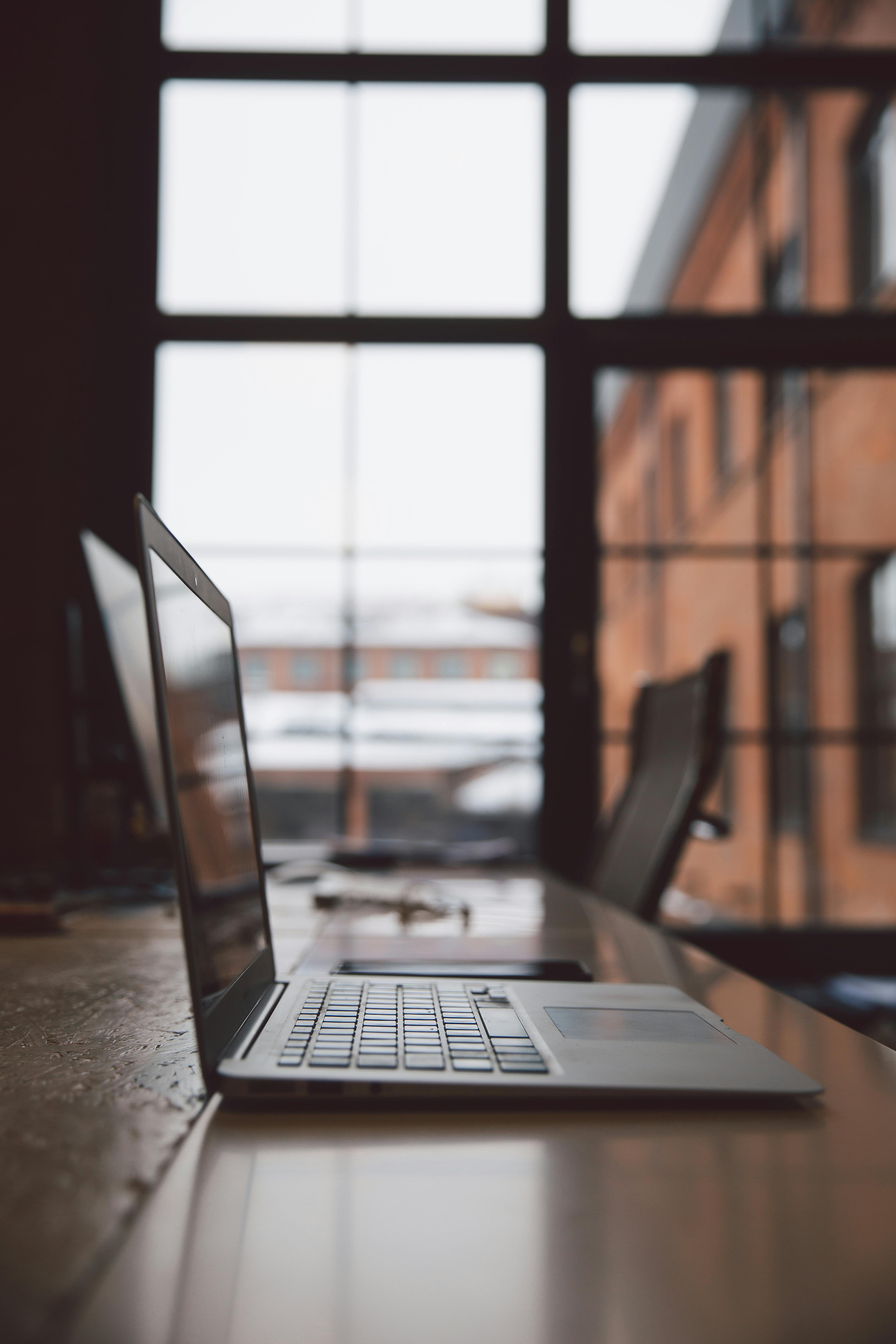 极简主义风格的办公室里，木桌上放着一台笔记本电脑，大窗户提供了充足的自然光线