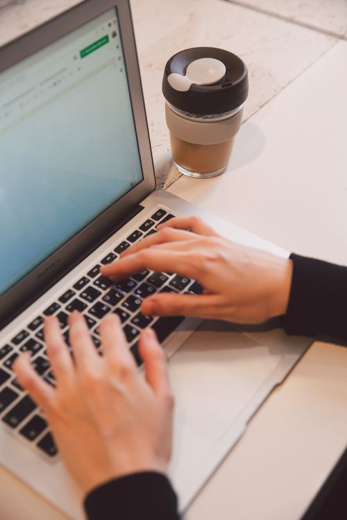 Free Focused individual typing on a laptop with a coffee cup beside, ideal for office and remote work themes. Stock Photo