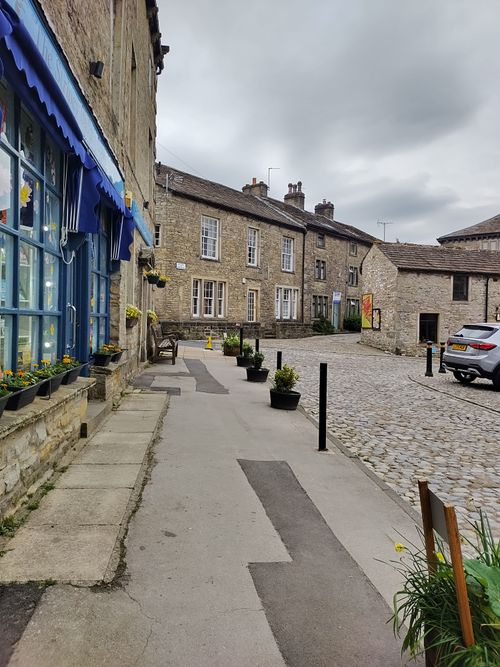 Free Quaint cobblestone street with stone buildings under cloudy skies, showcasing historic architecture. Stock Photo