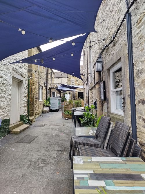 Free Quaint alleyway with outdoor seating, stone buildings, and blue shade sails. Stock Photo