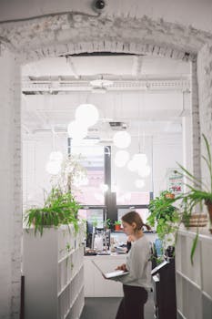 Contemporary office space with a woman working, featuring minimalistic design and lively plants.