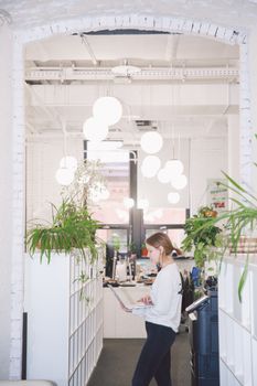 A woman works in a bright, modern office surrounded by plants and stylish lighting.