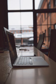 在现代办公空间里，一张带大窗户的木桌上，笔记本电脑被打开了