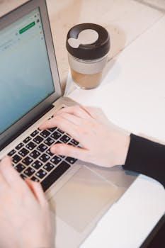 双手在笔记本电脑上打字，旁边放着咖啡杯，象征着远程工作与技术