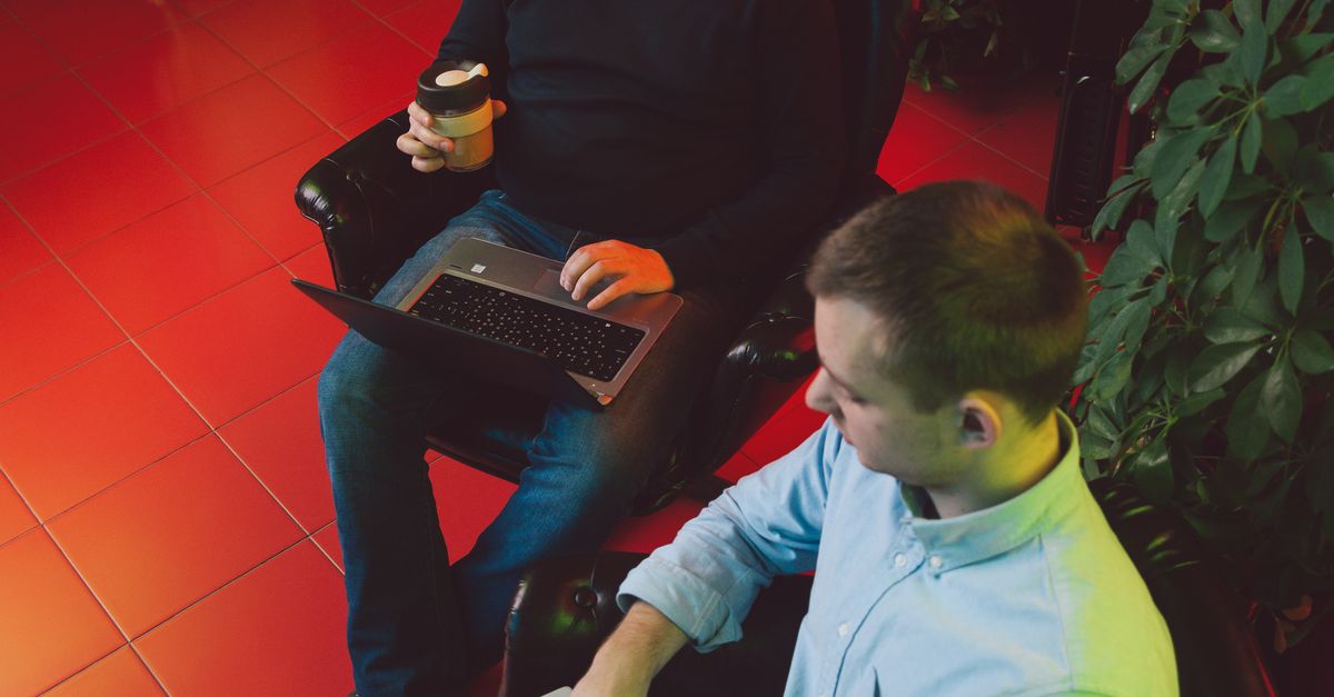 Photo by Polina Zimmerman Two men collaborating on laptops in an indoor garden with coffee.