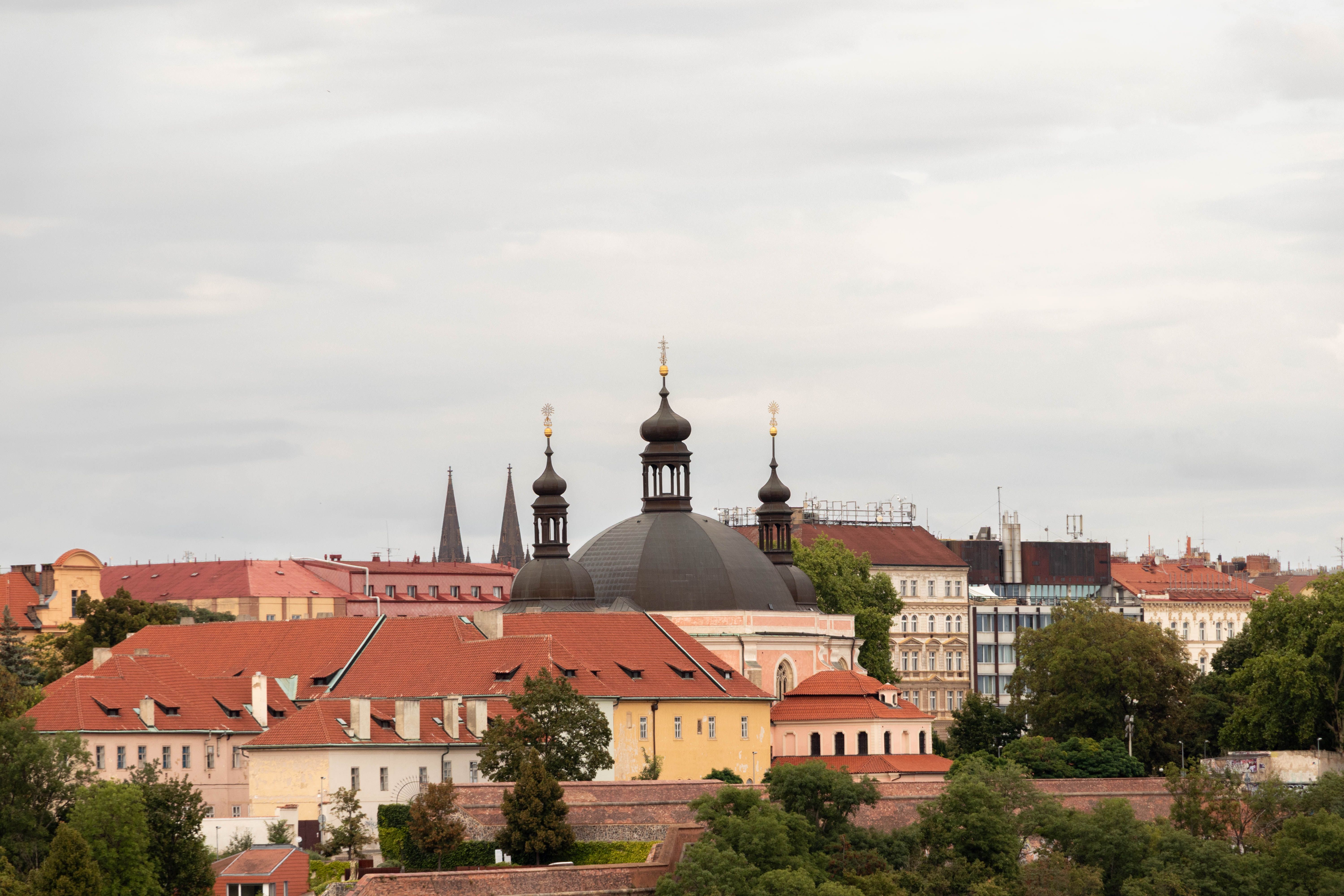 Capture of historic architecture in Prague showcasing domes and red tile roofs under an overcast sky.