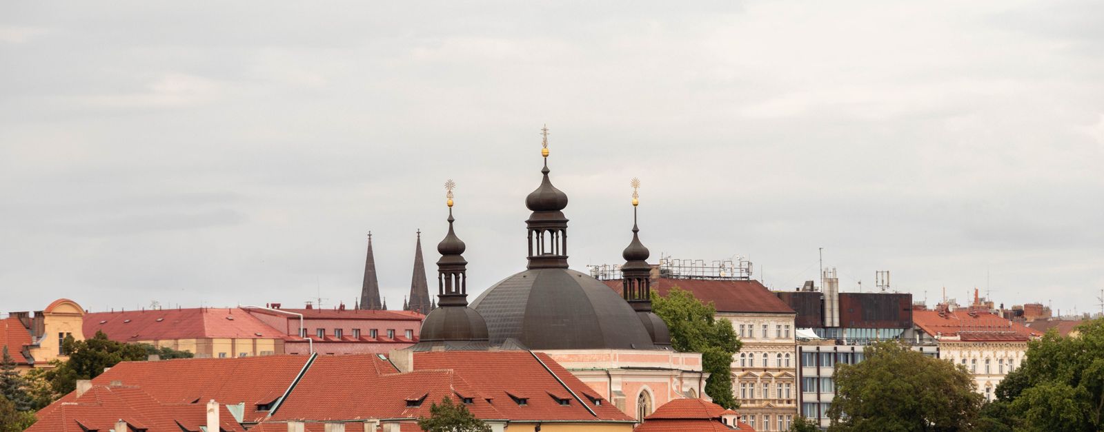 Capture of historic architecture in Prague showcasing domes and red tile roofs under an overcast sky.