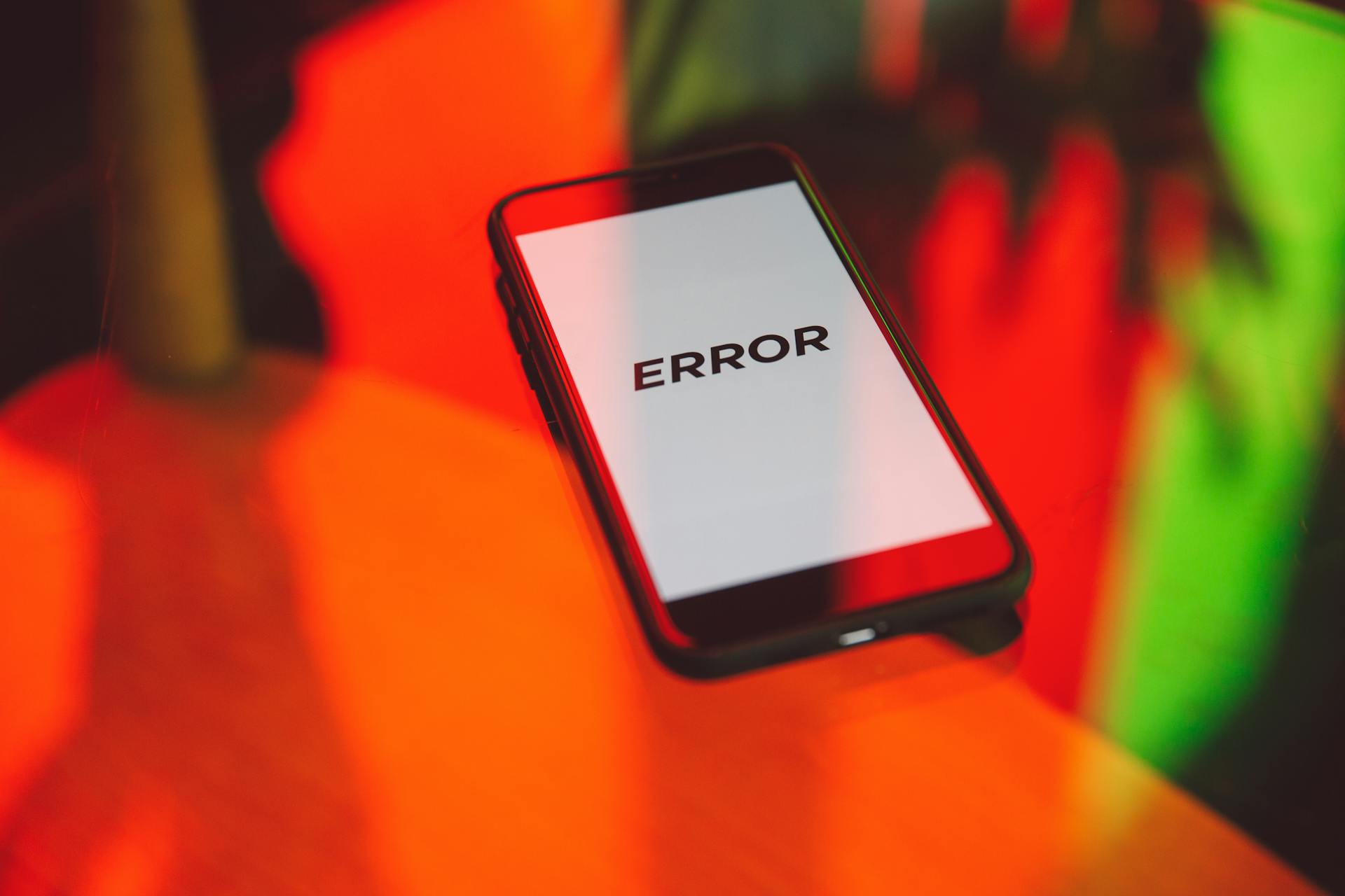 A smartphone displaying an 'ERROR' message surrounded by vibrant red and green reflections indoors.