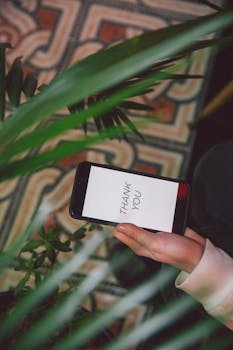 手持一部显示着“谢谢”信息的智能手机，周围环绕着郁郁葱葱的室内植物