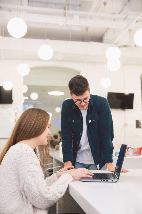 Free Two young adults collaborating over a laptop in a modern, bright office setting. Stock Photo