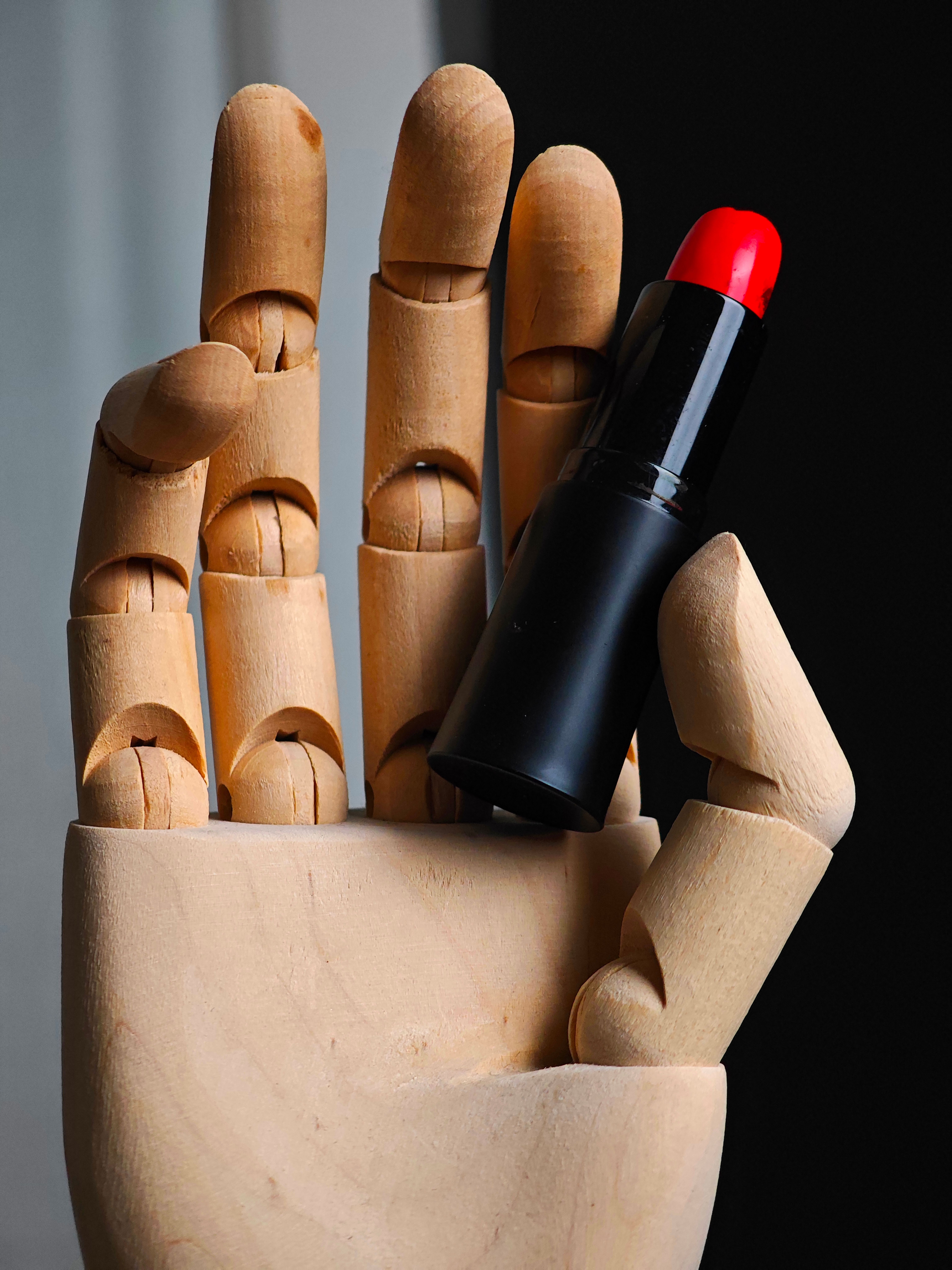 Detailed shot of a wooden hand model gripping a vibrant red lipstick, showcasing style and artistry.