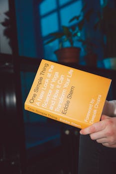 A person holding a yoga science book titled 'One Simple Thing' indoors.