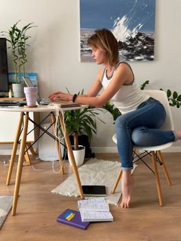 A focused woman works at home using a laptop in a modern, plant-filled workspace.