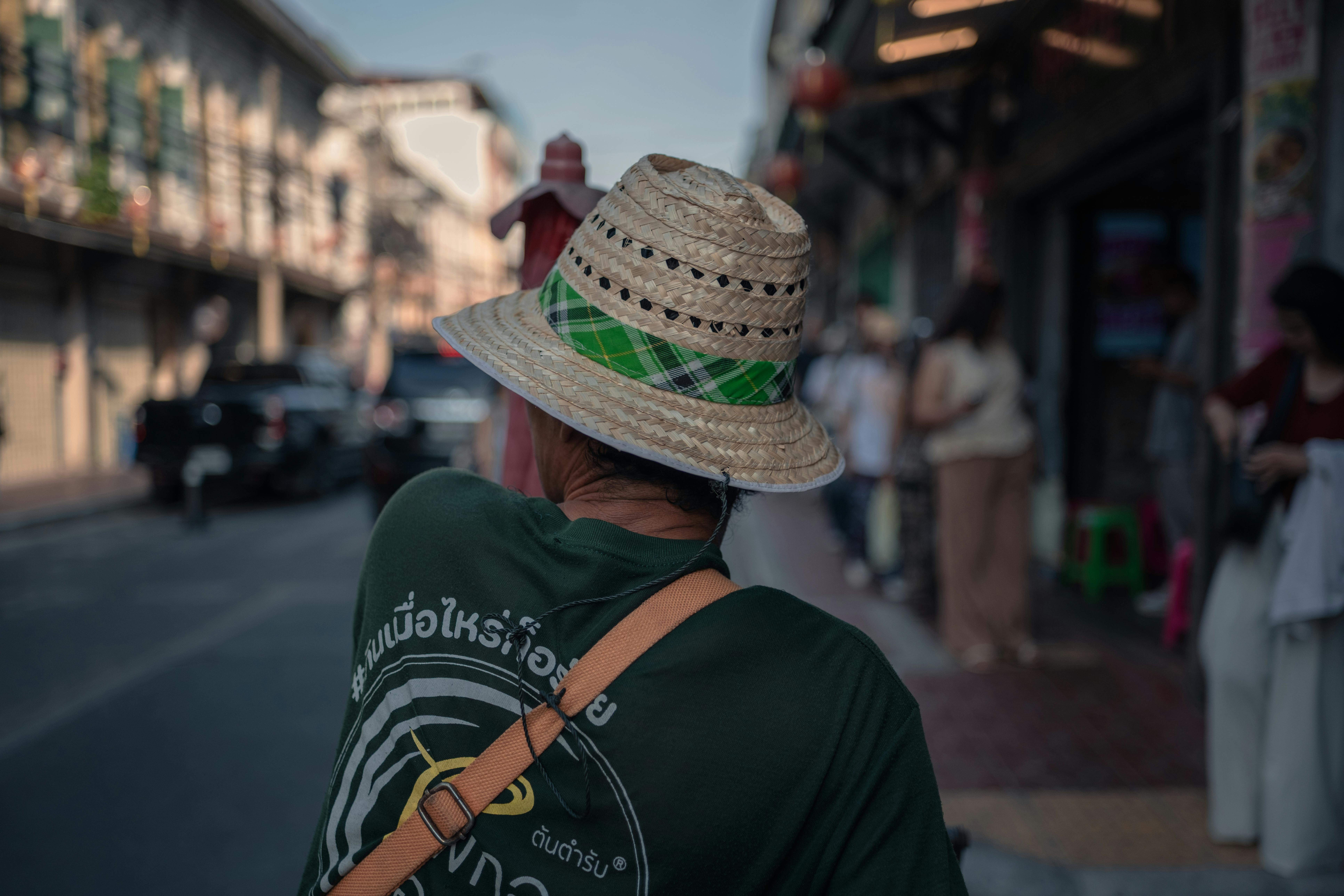 A person wearing a straw hat walks through an Asian market street on a sunny day.