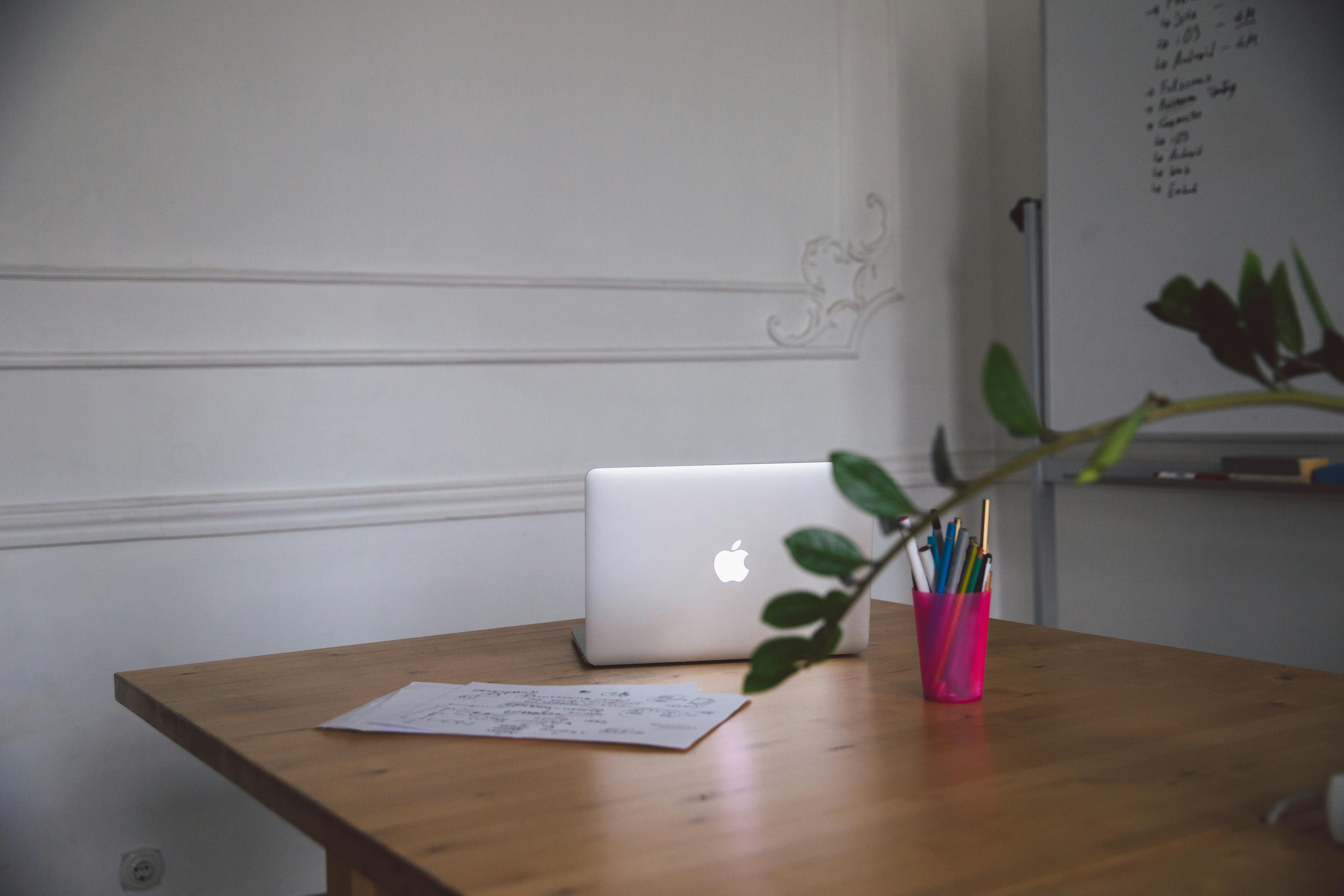A clean and minimalist office workspace with a laptop, paper, and pens on a wooden table.