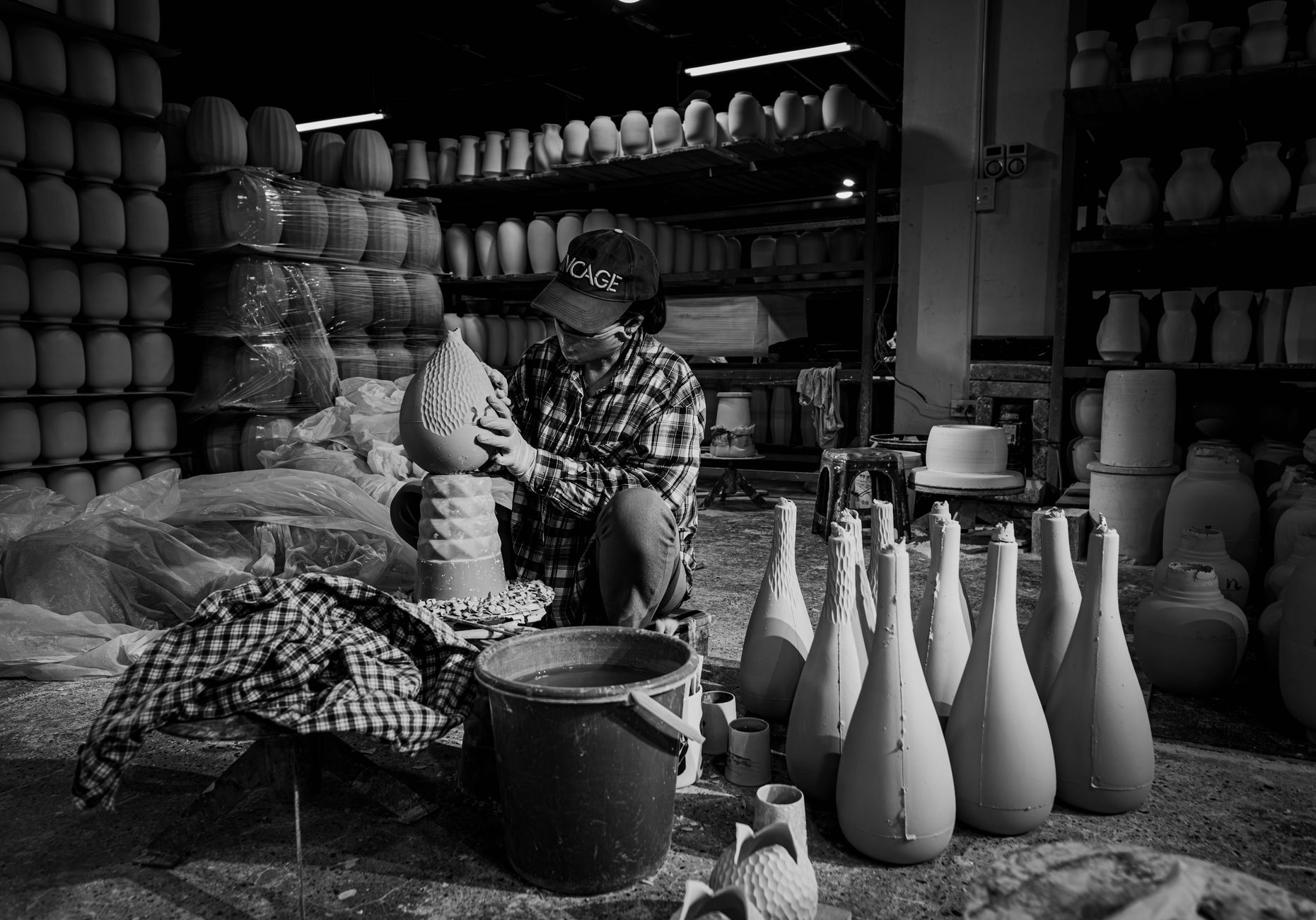 A skilled artisan carefully shaping pottery in a dimly lit workshop filled with ceramic vases.