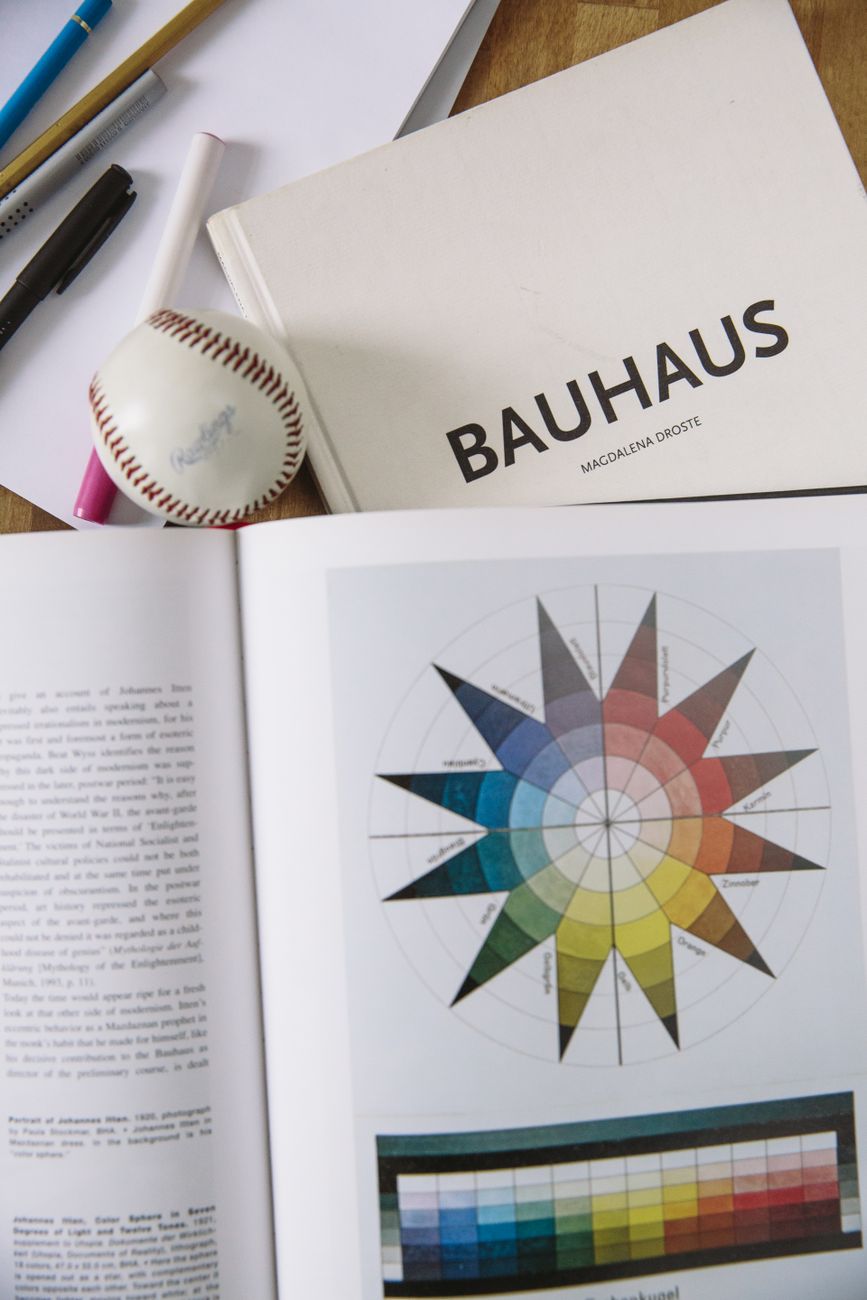 Open book with a Bauhaus color wheel, baseball, and pens on a table.. open, book, with