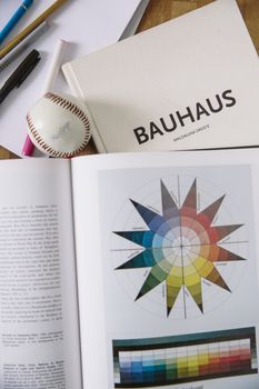 Open book with a Bauhaus color wheel, baseball, and pens on a table.. open, book, with