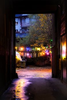 A vibrant alleyway illuminated by colorful lights during dusk, adding warmth to an urban setting.