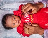 An adorable baby in red clothing holding hands with a parent adorned with henna design.