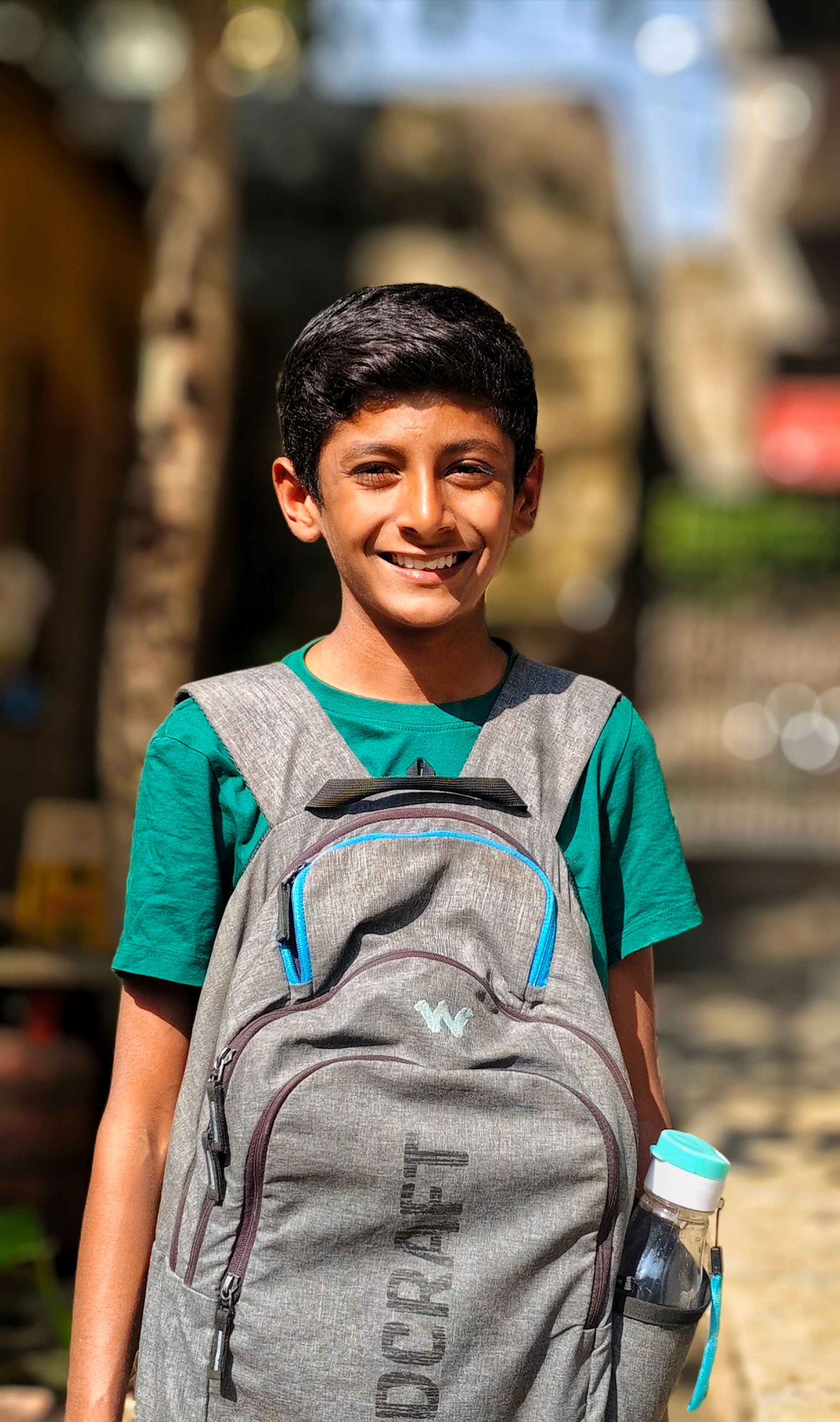 A cheerful young boy with a backpack, standing outdoors and ready for school.
