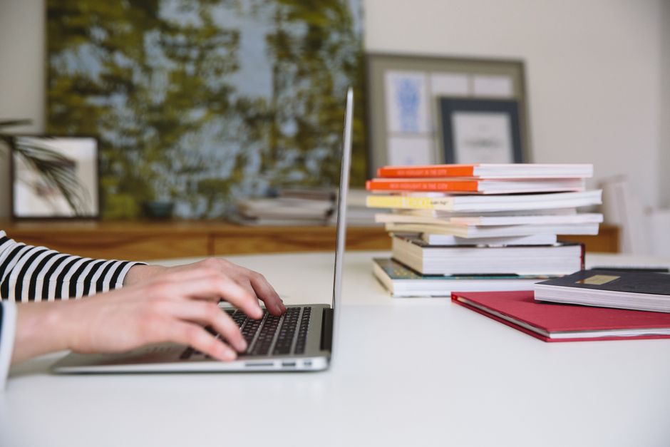 A person typing on a laptop surrounded by stacks of books, ideal for themes of studying and remote work.