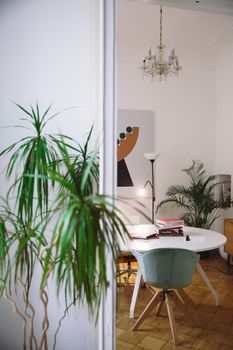 A stylish study room featuring a contemporary table, elegant chandelier, and lush houseplants.