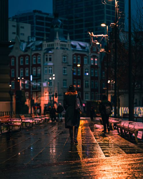 Free A person walks down a wet city street at night, surrounded by vibrant lights and historic buildings. Stock Photo
