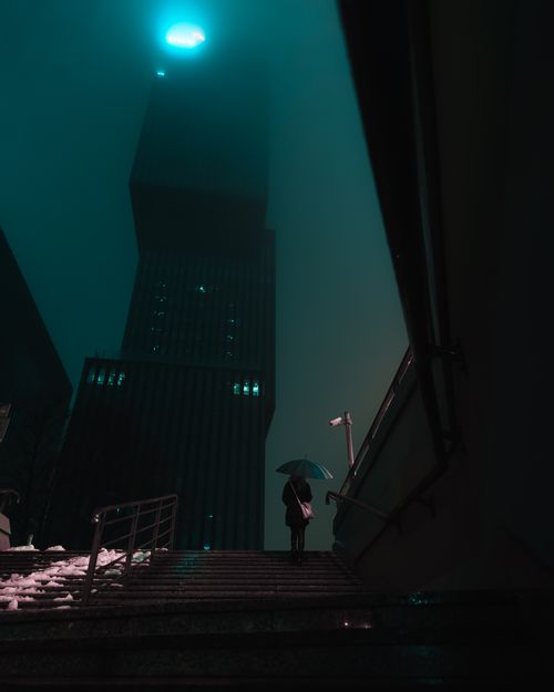 Free A solitary person with an umbrella in a moody urban night scene, surrounded by towering skyscrapers. Stock Photo