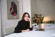 一位年轻女子坐在现代办公室的办公桌前，手里拿着笔记本电脑和鲜花，陷入了深思