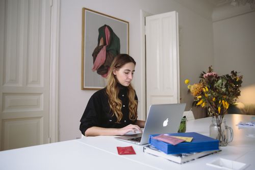 Free Young woman working on a laptop in a stylish home office space with floral decor. Stock Photo