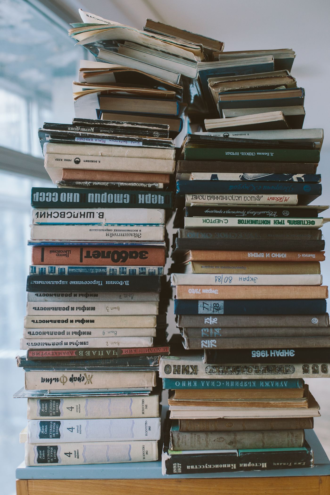 A tall stack of hardcover books arranged vertically on a plain surface