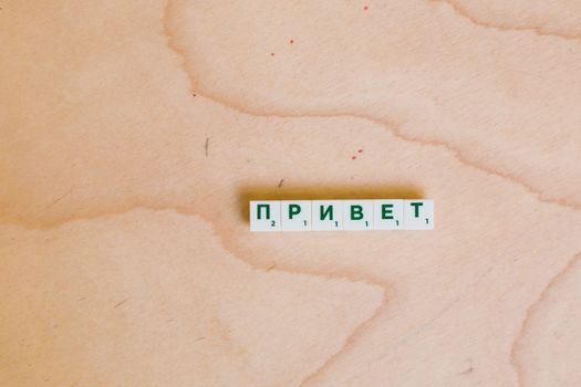 Scrabble tiles in Cyrillic spelling 'Hello' on a wooden surface.