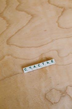 Russian Scrabble tiles spelling 'happiness' on wooden surface. Conceptual play and language piece.