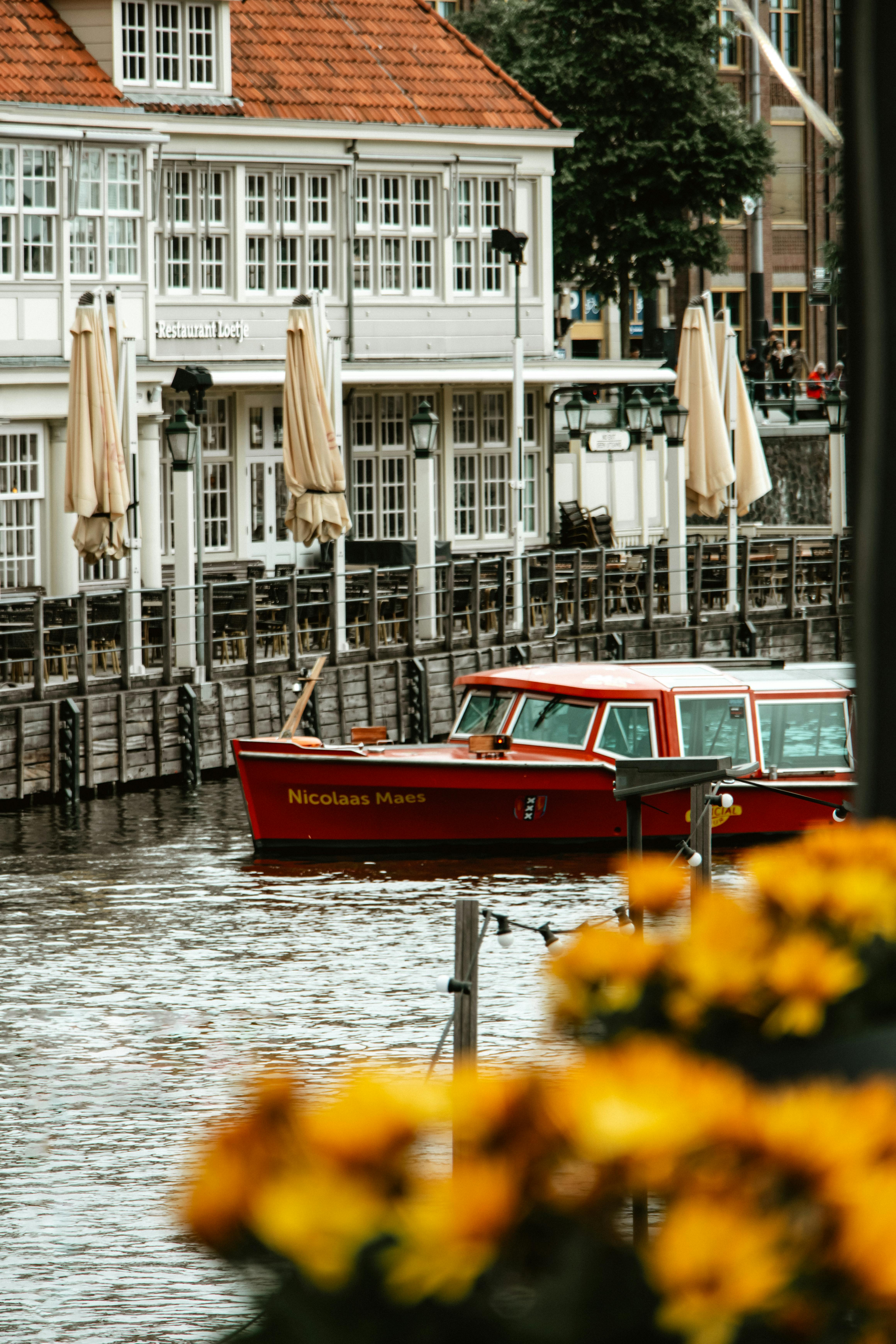 Red boat on Amsterdam canal with picturesque Dutch architecture in the background.