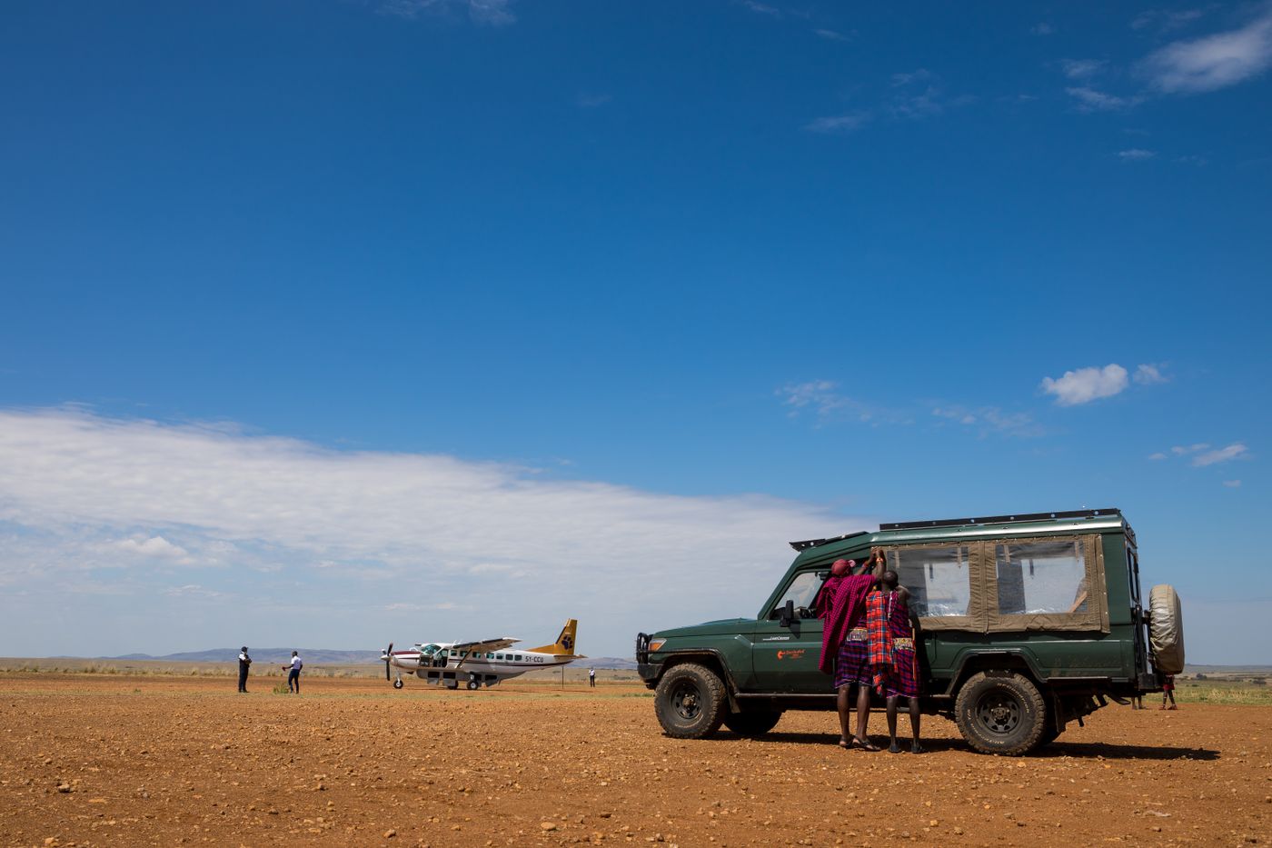 Safari vehicle and travellers at a remote airstrip in Kenya under a clear blue sky