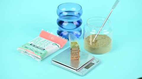 Herbal supplement setup with blate papes, jar, and digital scale on a blue background.