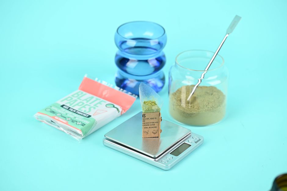 Herbal supplement setup with blate papes, jar, and digital scale on a blue background.