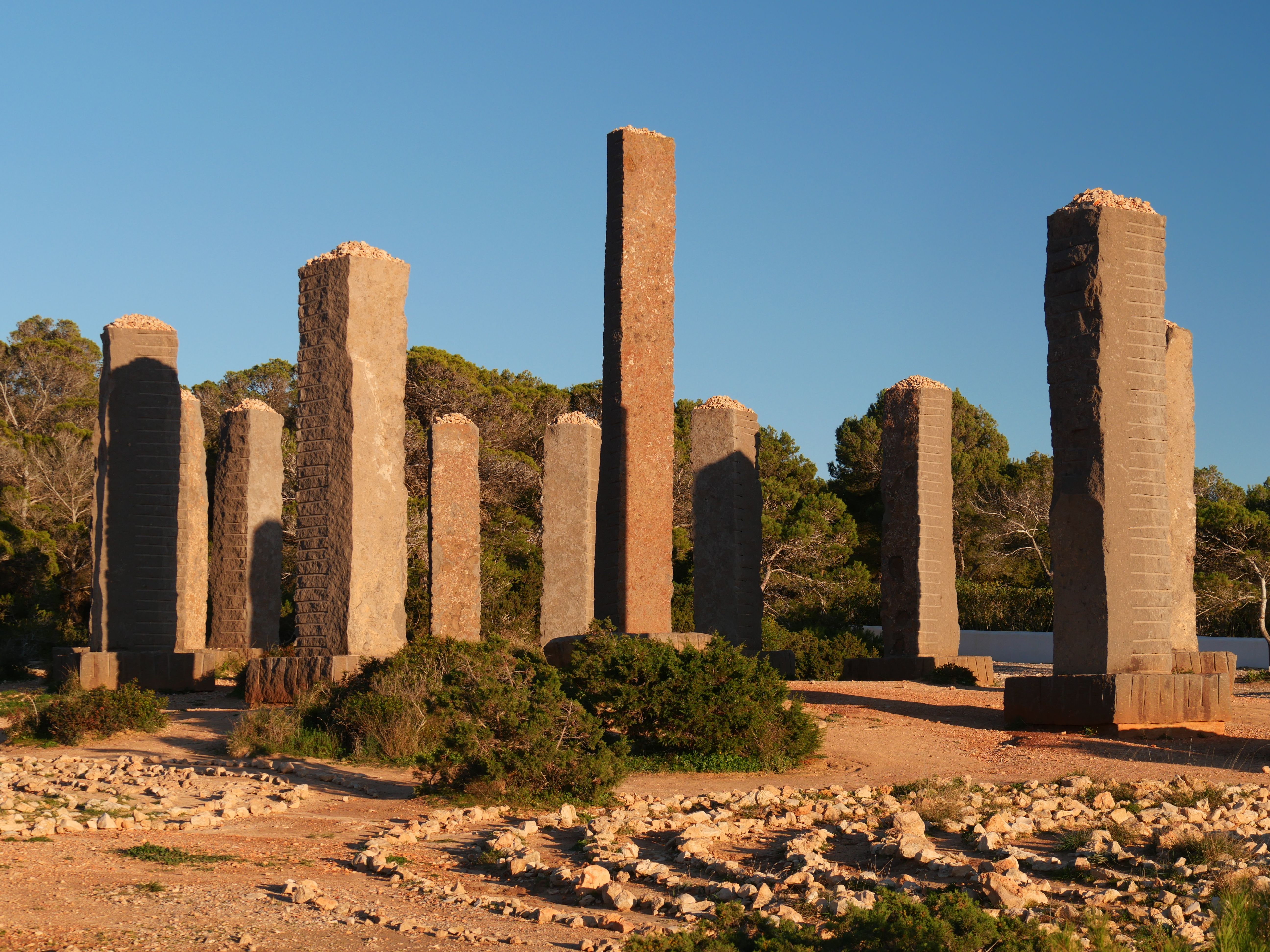 Ancient-like stone pillars standing in Ibiza, capturing a serene sunset with a clear blue sky backdrop.