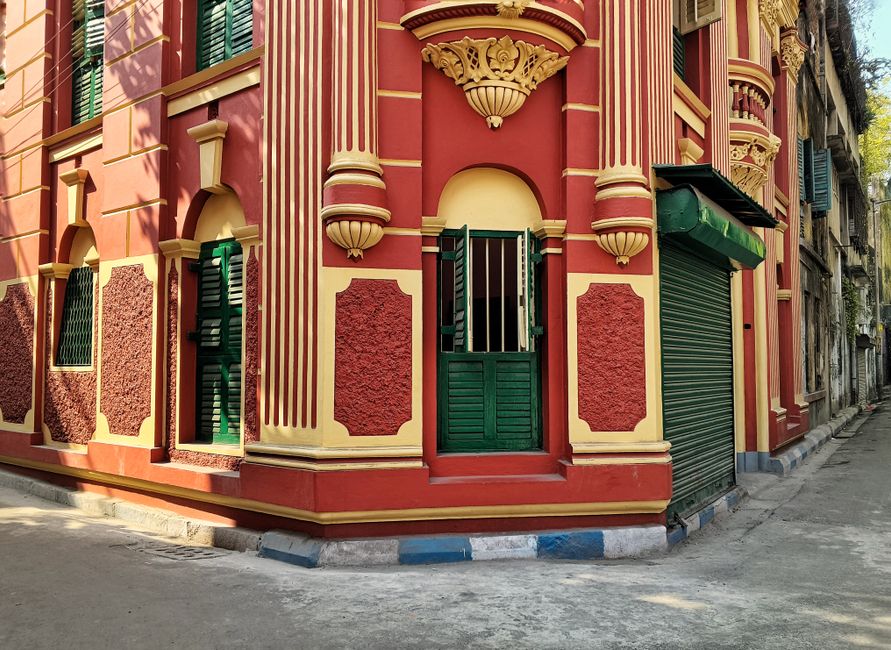 Vibrant red and yellow vintage building corner with ornate details and green shutters.