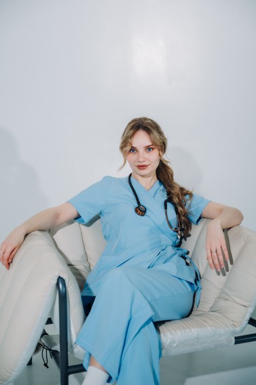 Free A nurse in blue scrubs and stethoscope sits confidently on a modern chair in a pristine setting. Stock Photo