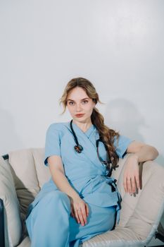 A female doctor in blue scrubs sits confidently with a stethoscope, embodying professionalism.