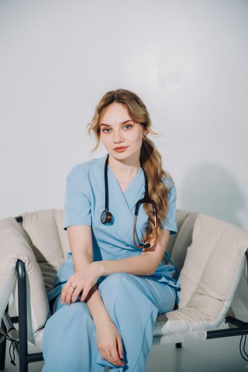 Free Portrait of a young female medical professional in blue scrubs, seated with a stethoscope around her neck. Stock Photo