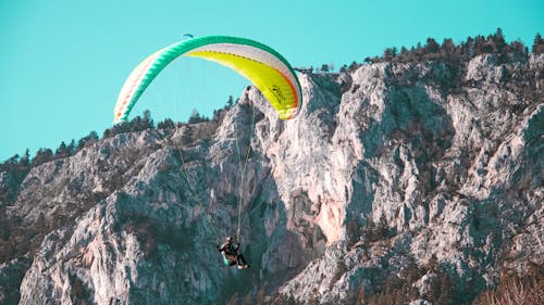Gratis Persona Che Guida Il Paracadute Verde E Giallo Sopra La Montagna Rocciosa Grigia Foto a disposizione