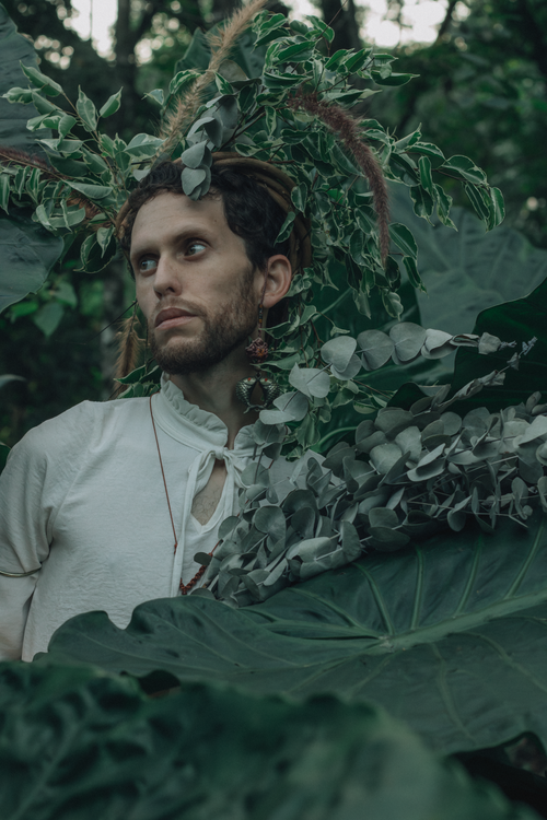 Free Man blending into lush greenery with unique headdress, serene expression. Stock Photo