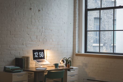 Minimalist desk setup with laptop, typewriter, and large window in a bright room.