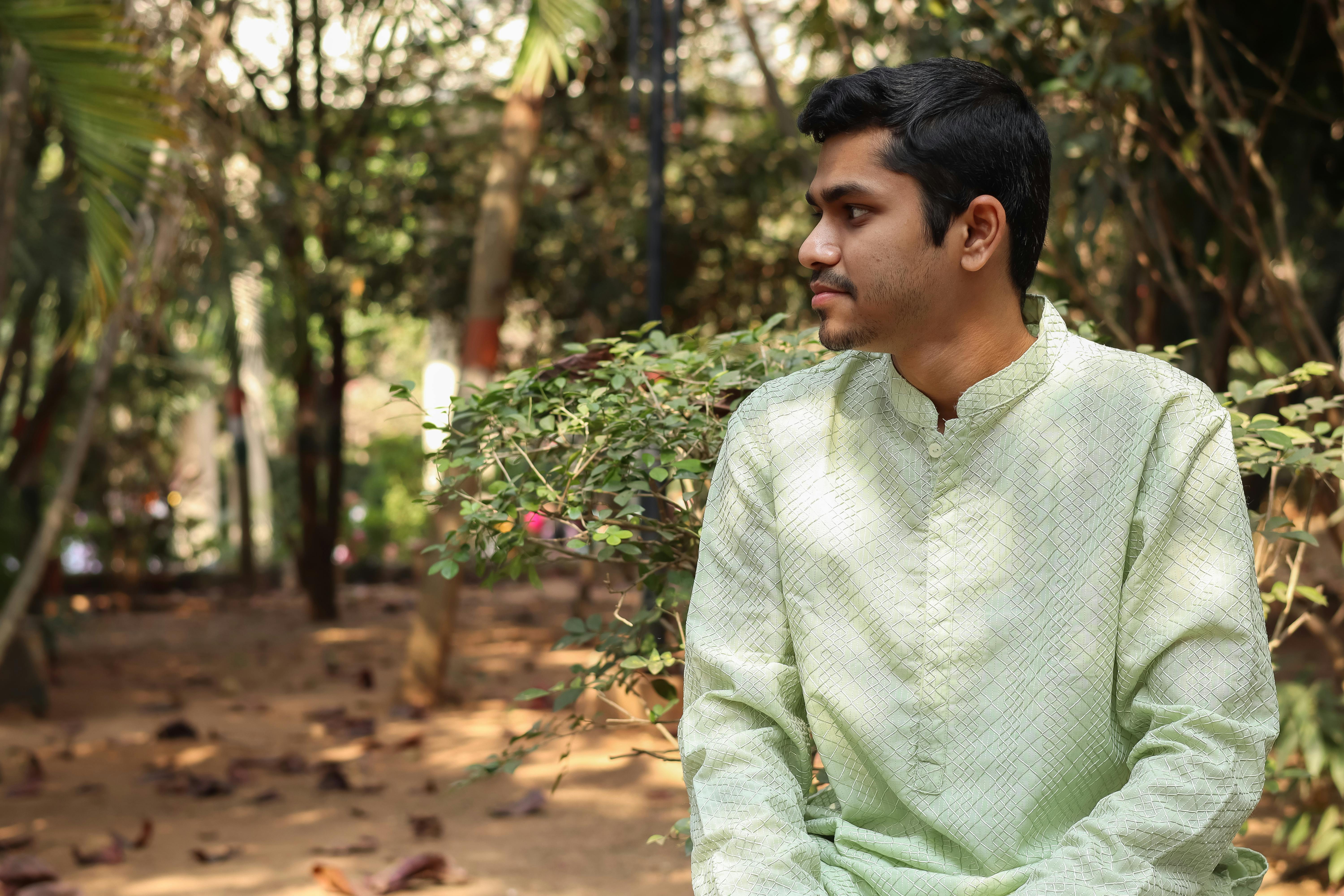 A young man in traditional Indian attire sits in a park, expressing calmness and tranquility.