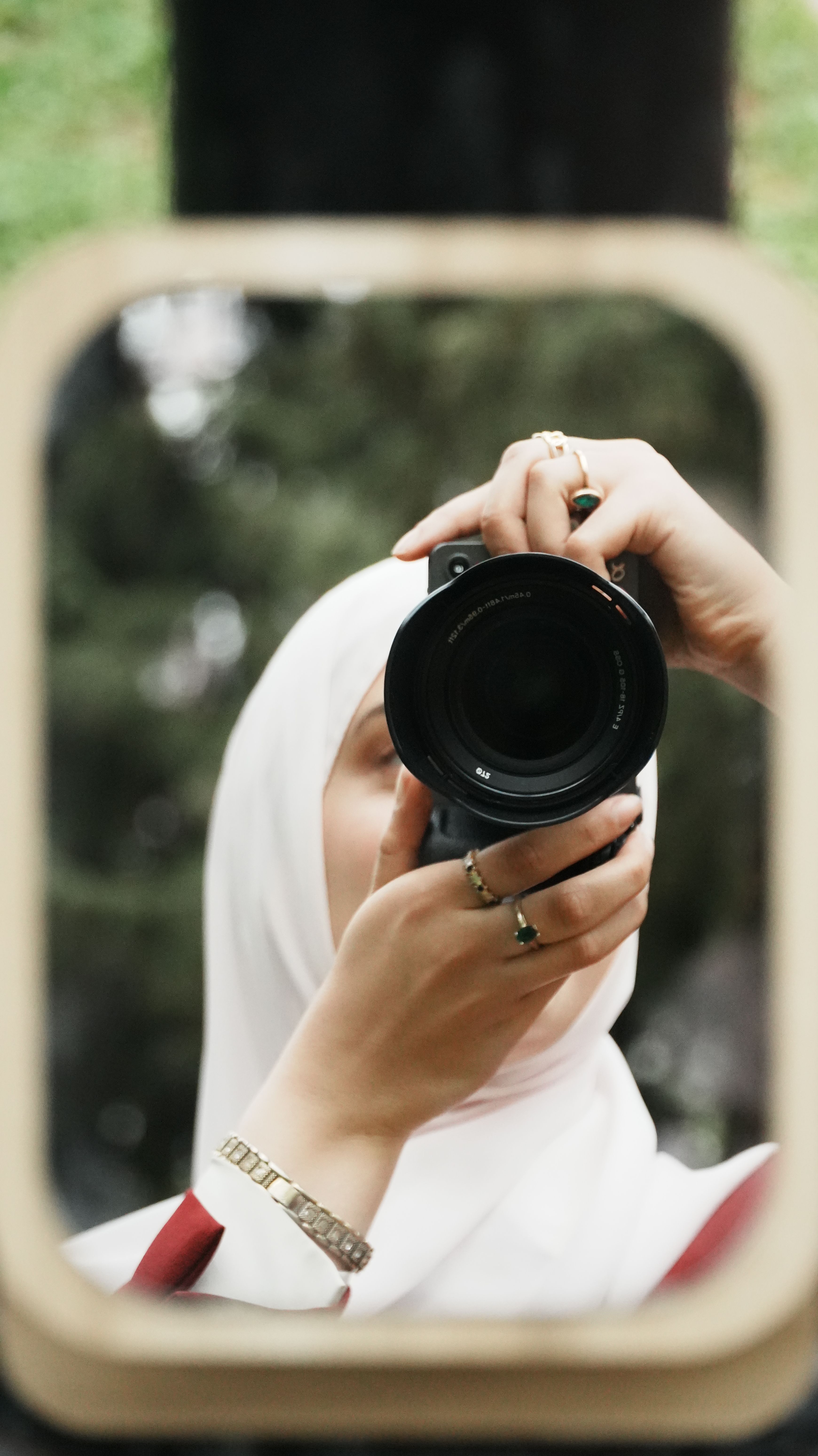 A woman in a hijab takes a photo of her reflection using a professional camera.