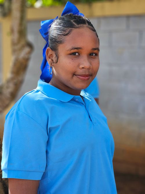 Free A young woman wearing a blue shirt smiles while standing outside on a sunny day. Stock Photo
