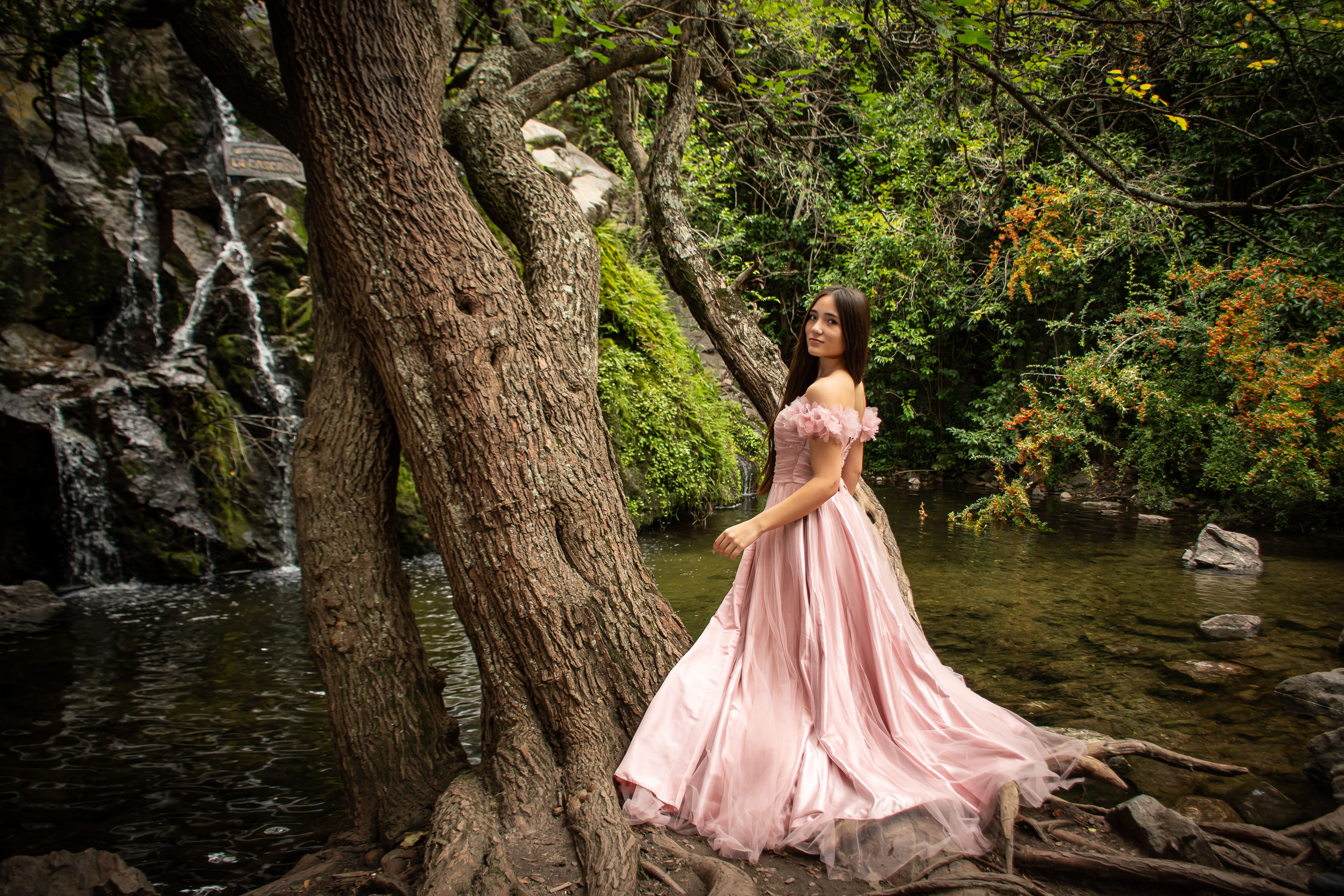 Woman in pink dress amidst a serene forest stream, exuding elegance and tranquility.